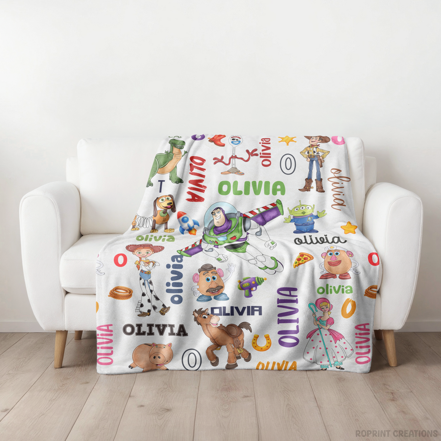 A white personalized blanket with colorful Toy Story characters and the name 'OLIVIA' repeated, draped over a white armchair in a bright room.